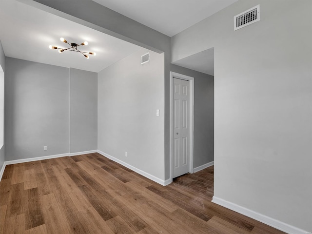 empty room featuring an inviting chandelier, visible vents, wood finished floors, and baseboards