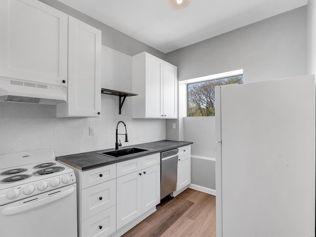 kitchen with white appliances, light wood-style flooring, under cabinet range hood, dark countertops, and a sink