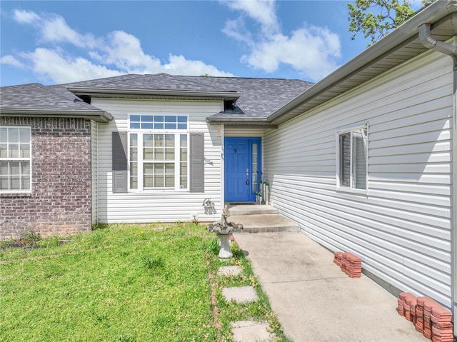 entrance to property with roof with shingles and a lawn