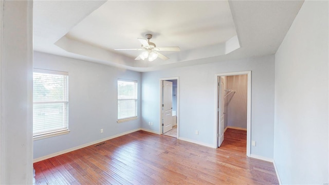 unfurnished bedroom with light wood-type flooring, a tray ceiling, visible vents, baseboards, and a spacious closet