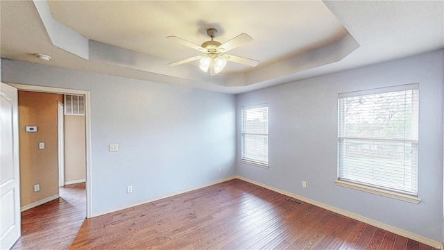 empty room featuring a raised ceiling, visible vents, baseboards, wood finished floors, and a ceiling fan