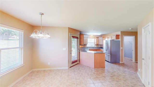 kitchen with a sink, a chandelier, decorative light fixtures, a peninsula, and freestanding refrigerator