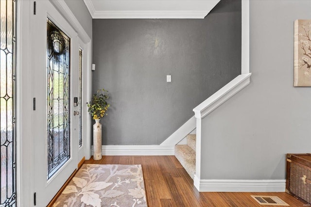 foyer with wood finished floors, visible vents, ornamental molding, baseboards, and stairs