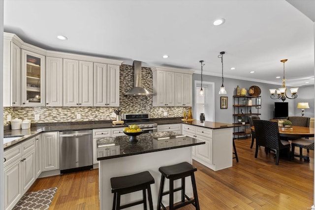 kitchen featuring wall chimney exhaust hood, crown molding, decorative backsplash, a peninsula, and appliances with stainless steel finishes