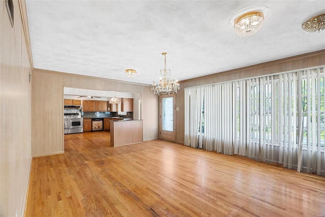 unfurnished living room with wood walls, visible vents, light wood-type flooring, and a notable chandelier