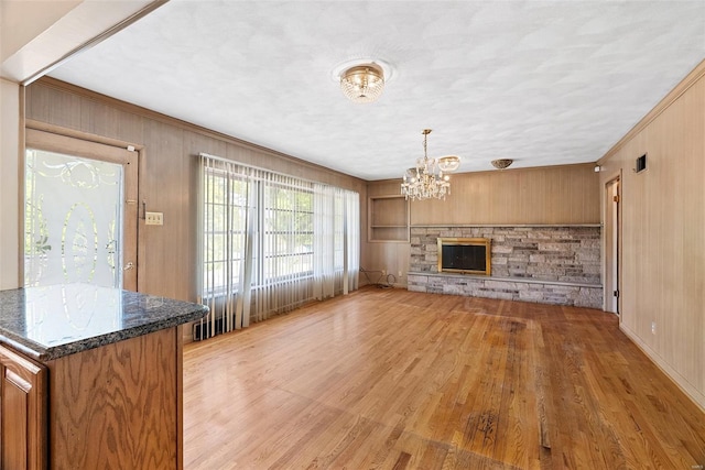 unfurnished living room with wood walls, light wood-style floors, crown molding, and a notable chandelier
