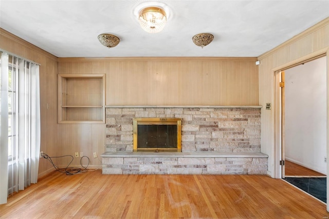 unfurnished living room with built in features, wooden walls, a stone fireplace, baseboards, and wood finished floors
