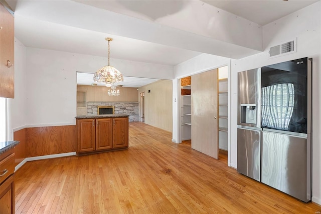 kitchen with stainless steel fridge with ice dispenser, brown cabinets, light wood finished floors, visible vents, and a notable chandelier