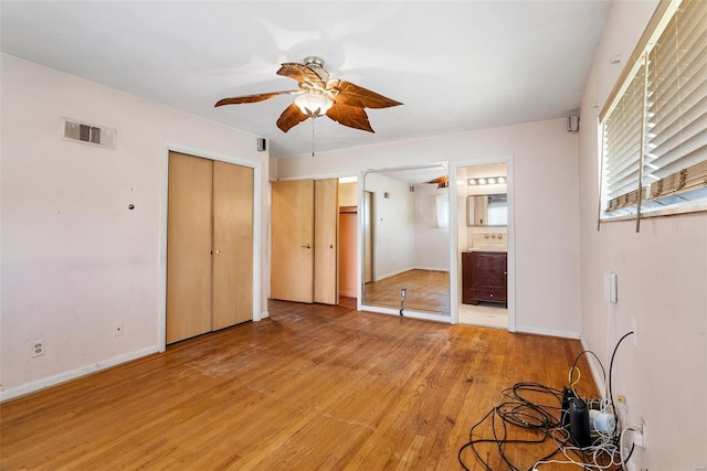 unfurnished bedroom featuring ensuite bath, light wood-style floors, baseboards, visible vents, and a ceiling fan