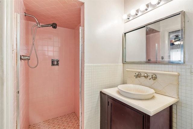 bathroom featuring a tile shower, vanity, wainscoting, and tile walls