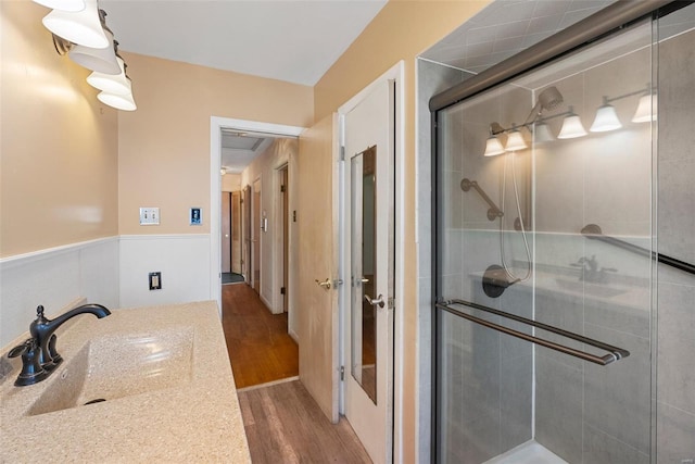 bathroom with a wainscoted wall, a sink, a shower stall, and wood finished floors