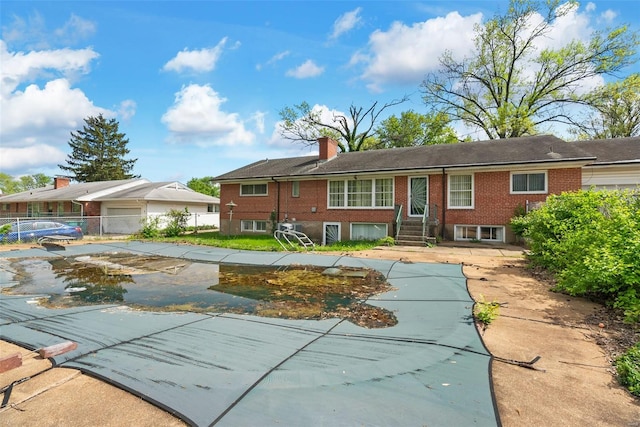 rear view of house with brick siding, a chimney, entry steps, and fence