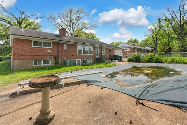 back of property with fence, a chimney, a covered pool, and brick siding