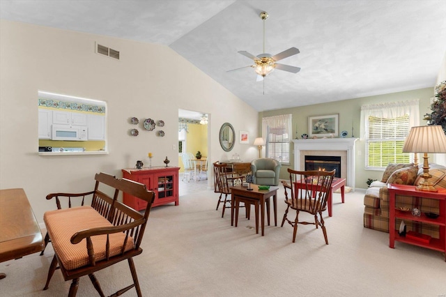 living room featuring light carpet, vaulted ceiling, visible vents, a glass covered fireplace, and ceiling fan
