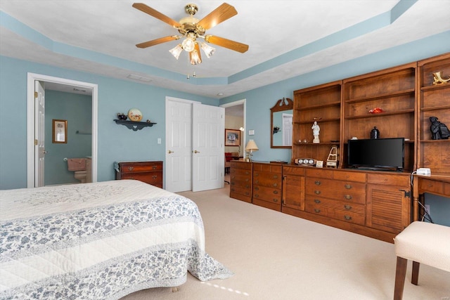 bedroom featuring light carpet, ensuite bathroom, visible vents, and a raised ceiling