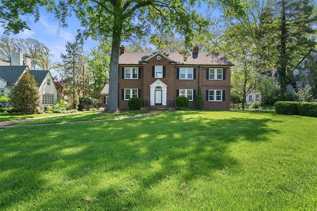 colonial-style house featuring brick siding, a chimney, and a front yard