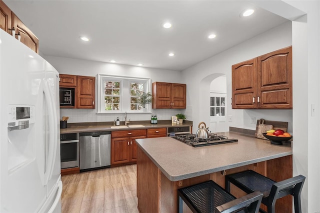 kitchen featuring a kitchen bar, arched walkways, brown cabinets, a sink, and black appliances