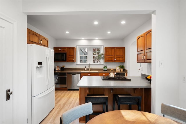 kitchen featuring a kitchen bar, brown cabinets, a sink, a peninsula, and stainless steel appliances
