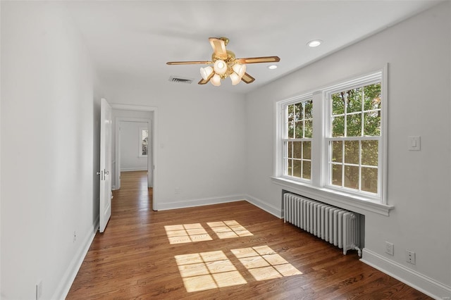 unfurnished room featuring visible vents, a ceiling fan, radiator heating unit, and wood finished floors