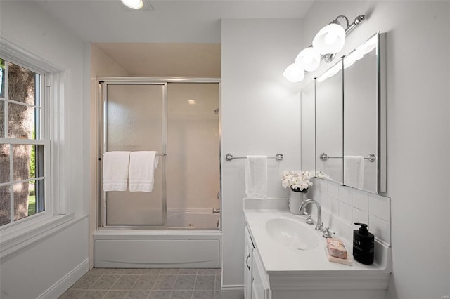 bathroom with vanity, enclosed tub / shower combo, baseboards, and a wealth of natural light