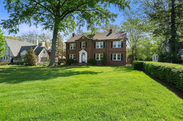 colonial-style house featuring brick siding, a chimney, and a front yard