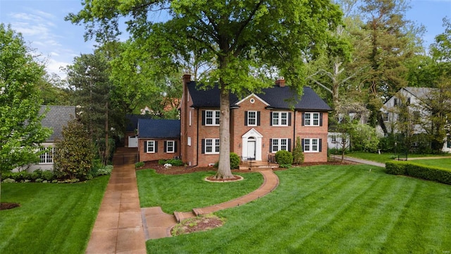 colonial-style house with a chimney, a front lawn, and brick siding