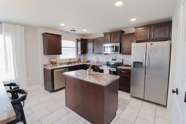 kitchen featuring light stone counters, stainless steel appliances, dark brown cabinets, a sink, and a center island