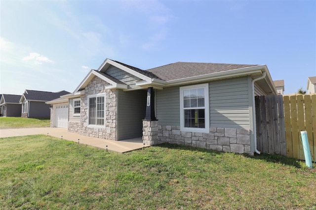 view of front of house with stone siding, fence, a front yard, and a garage
