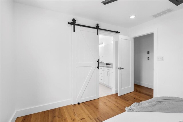 bedroom with visible vents, a barn door, baseboards, connected bathroom, and light wood-style flooring