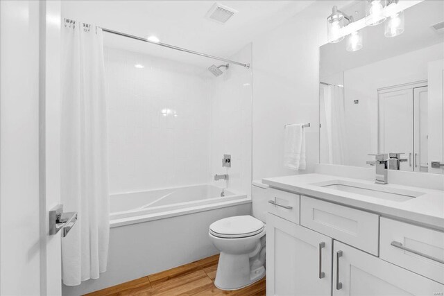 full bathroom with vanity, shower / tub combo with curtain, visible vents, wood finished floors, and toilet