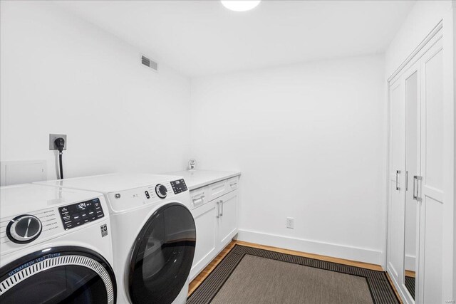 washroom featuring visible vents, wood finished floors, cabinet space, baseboards, and separate washer and dryer