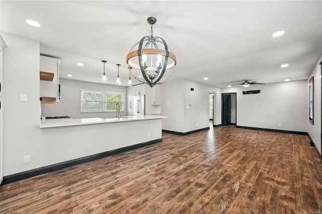 unfurnished living room featuring ceiling fan with notable chandelier, dark wood finished floors, recessed lighting, a sink, and baseboards