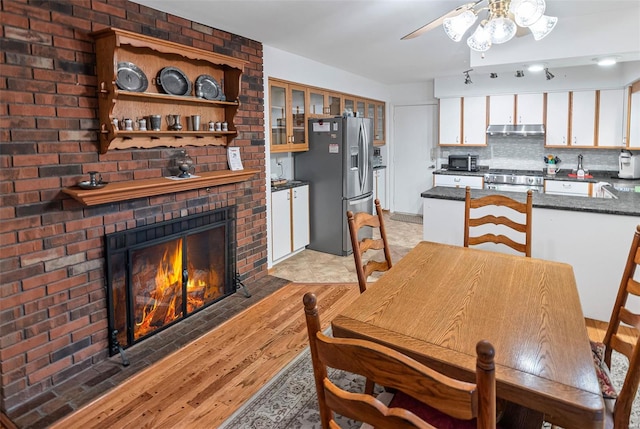 dining room featuring a brick fireplace, a ceiling fan, and light wood finished floors