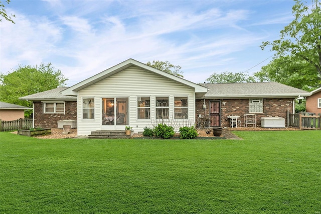 back of house featuring a lawn, a hot tub, and brick siding