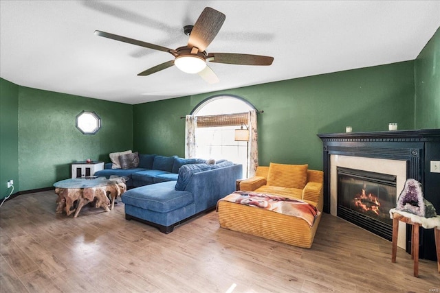 living area featuring a glass covered fireplace, plenty of natural light, a ceiling fan, and wood finished floors