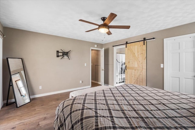 bedroom with a barn door, baseboards, wood finished floors, and ceiling fan
