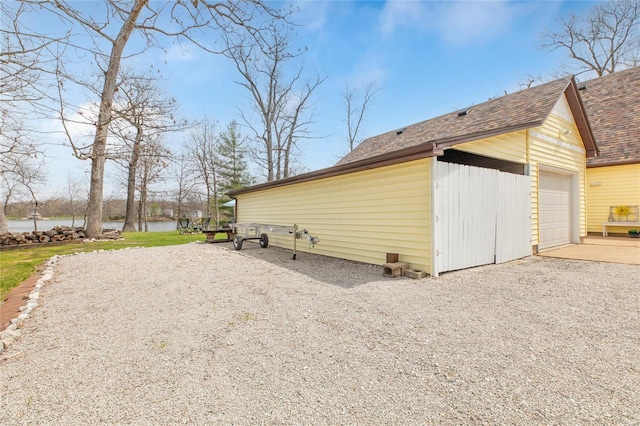 view of side of property featuring an outdoor structure, a water view, roof with shingles, gravel driveway, and a garage