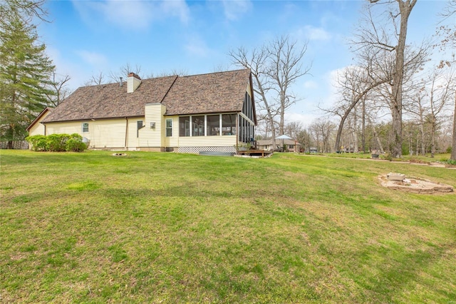 rear view of house with a sunroom, roof with shingles, a yard, and a chimney