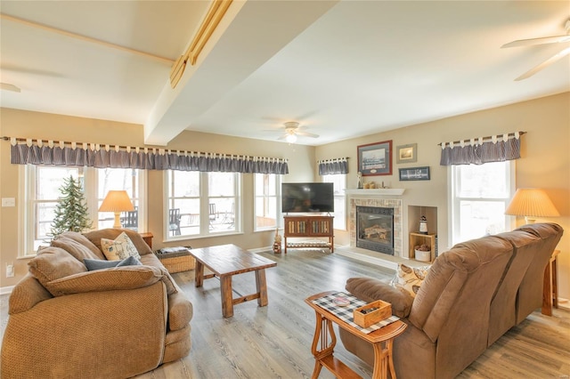 living area with a glass covered fireplace, light wood finished floors, baseboards, and ceiling fan