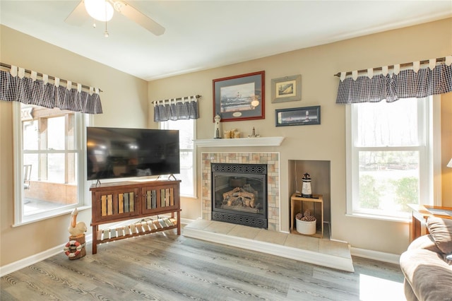 living room featuring baseboards, a ceiling fan, a tile fireplace, and wood finished floors