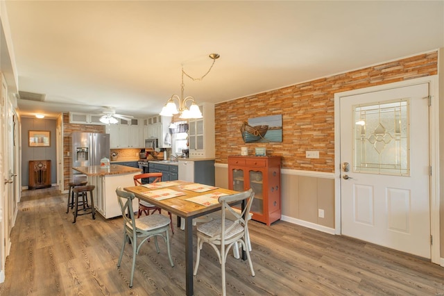 dining area with light wood-type flooring, ceiling fan with notable chandelier, wainscoting, and visible vents