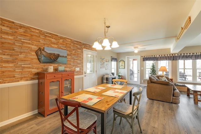dining space with light wood-style floors, ceiling fan with notable chandelier, and a wainscoted wall