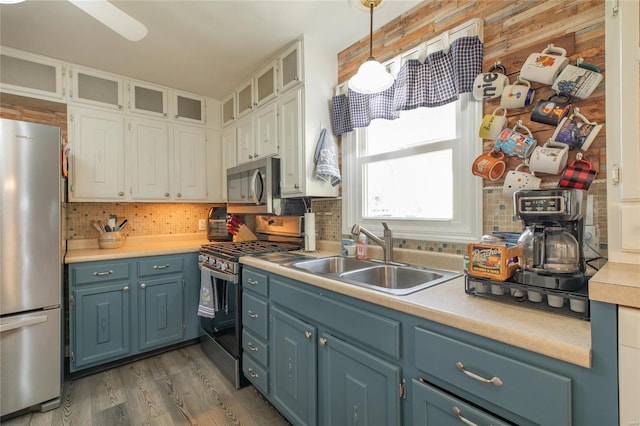 kitchen with blue cabinetry, light countertops, a sink, stainless steel appliances, and backsplash