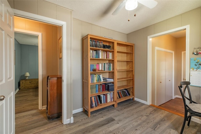 living area with a decorative wall, ceiling fan, and wood finished floors