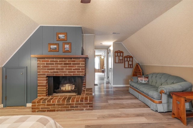 living area with vaulted ceiling, a textured ceiling, visible vents, a decorative wall, and wood finished floors