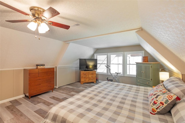 bedroom featuring ceiling fan, light wood-style flooring, a textured ceiling, visible vents, and lofted ceiling