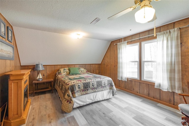 bedroom with wooden walls, visible vents, wood finished floors, and lofted ceiling