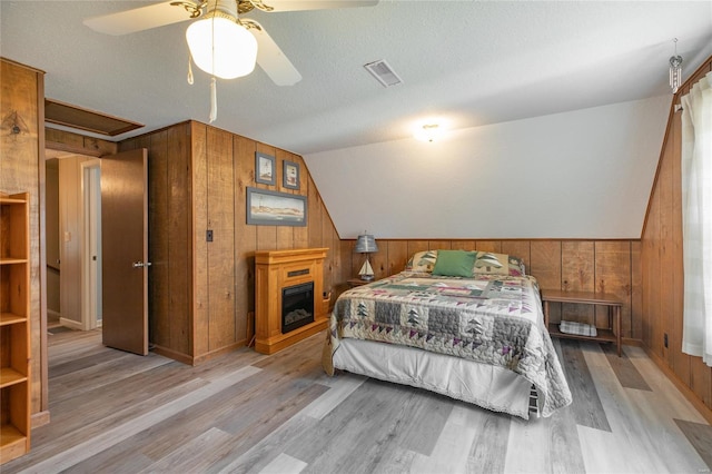 bedroom with wood walls, lofted ceiling, visible vents, and wood finished floors