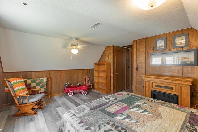 bedroom with a textured ceiling, wood walls, visible vents, lofted ceiling, and wood finished floors