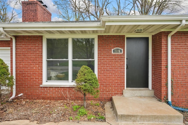 property entrance with a chimney and brick siding